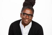 Black woman with hair up in a professional attire wearing black-rimmed glasses